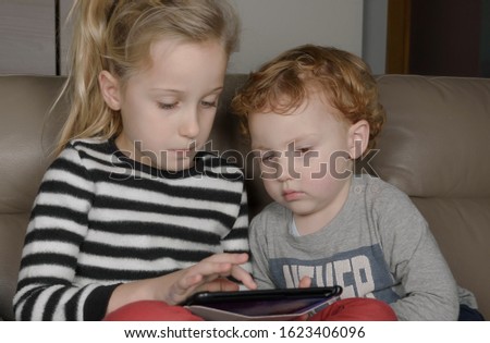 Kids sitting in sofa and playing with tablet. Sister and brother have fun with digital tablets on sofa at home. Communication and family friendship concept.
