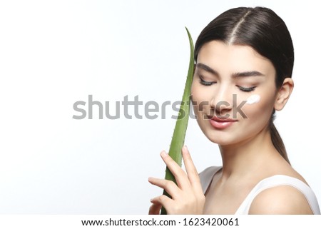 Perfect face of asian girl holding a leaf of green aloe. Very beautiful woman with healthy, clean skin and aloe vera leaves. Skin care product offer. applying cream on a clean face. Banner for text
