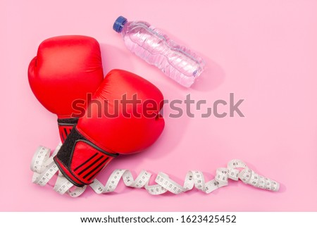 Fitness, weight loss or exercise concept. Boxing gloves, mineral water and measure tape isolated on pink background. Copy space