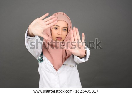 Gesturing finger frame. Portrait of smiling beautiful young muslim doctor woman looking at camera and gesturing finger frame while standing indoors.