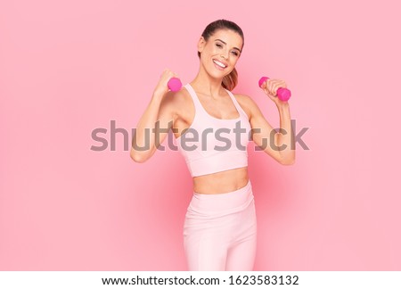 Happy fit Woman Doing an Exercise with dumbbell Over Pink Studio Background. Smiling girl. Fitness Workout. Healthy lifestyle concept.
