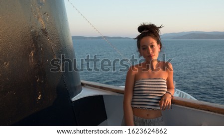 Closeup of Asian teen in striped tube top leaning against railing   on ferry boat going to Greece