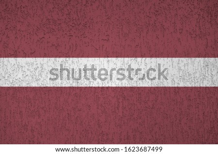 Latvia flag depicted in bright paint colors on old relief plastering wall close up. Textured banner on rough background