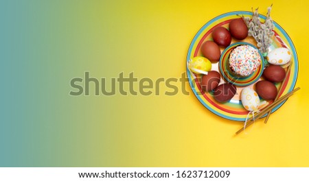 Greeting Easter background with a plate, painted Easter eggs, candles and willow branches. The concept of an Easter greeting card banner on a bright yellow and blue background top view.