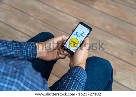 5g network danger concept. Man checking his smartphone with 5g network and warning sign displayed on the phone.