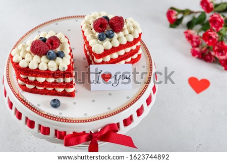 Red velvet cake in heart shape on St. Valentines Day with red roses on white background. Bakery, confectionery concept. Sweet present. Close up