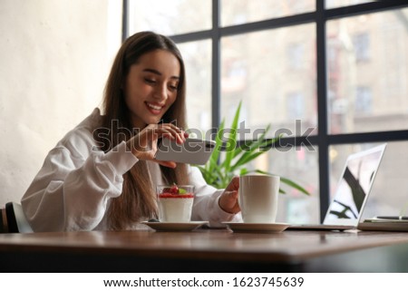 Young blogger taking picture of dessert at table in cafe