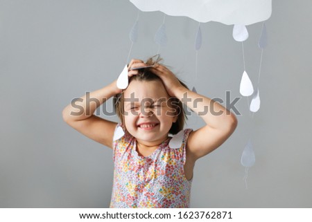 conceptual photo happiness in any weather, emotional girl child in a summer dress under paper rain, raindrops from paper over a funny Caucasian child. Cloudless happy childhood