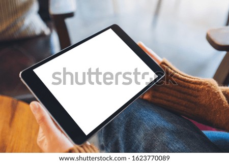 Mockup image of a woman sitting and holding black tablet pc with blank white desktop screen 