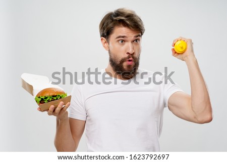 A man with a hamburger a white T-shirt and mustard in a yellow jar