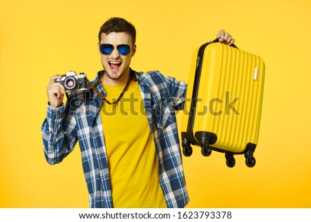 Plaid shirt sunglasses traveler with a camera and a yellow suitcase