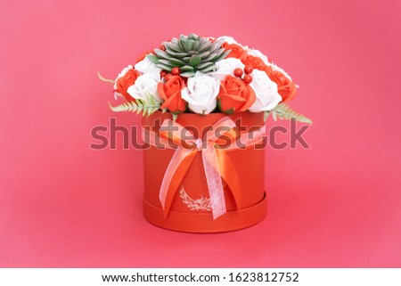 Flowers in bloom: A bouquet of red and white roses in a red round box on a pink background.
