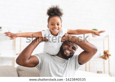 Happy afro family little daughter and father having fun together at home, imitating airplane