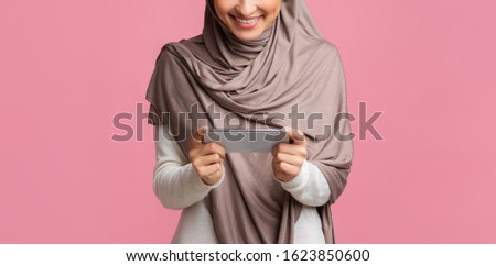 Modern smartphone in horizontal orientation in hands of unrecognizable muslim woman in hijab. Islamic girl browsing videos or media on her device