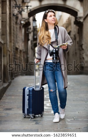 Smiling young happy tourist blond girl taking a walk in the town with her travel bag 
