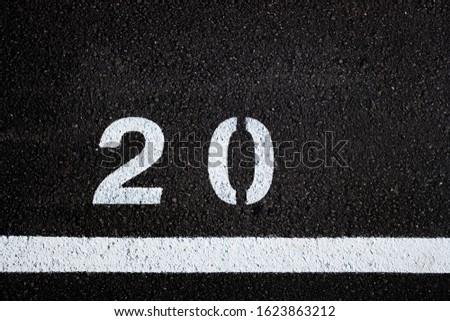 Number 20, painted on the paved ground of a parking lot with white paint.