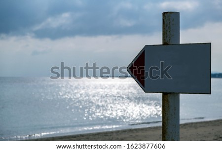 White empty , blank metal sign on rusty pole shows the direction to the sea. Sunbeams through clouds make sea's surface glittering. Blur background, copyspace