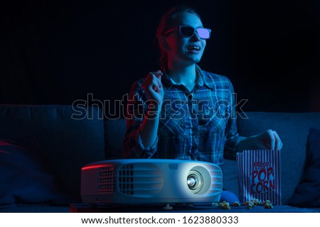 Girl watching a movie. Watching movies in 3D, with glasses. Cinema for home, relaxation and fun. Popcorn. Creative light.