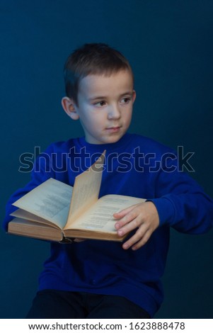 Studio portrait of boy on blue background in a classic t-shirt. Holding a book.