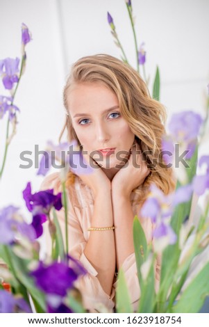 Attractive young girl with blond curly hair and beautiful make-up in a delicate blond chiffon blouse with blue irises on a white background
