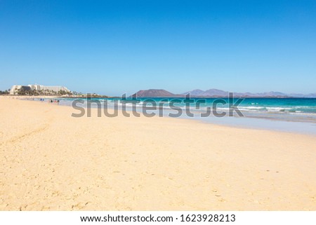 Beach hotel on Fuerteventura canary islands with the beach in front and the sea water with blue azure aquamarine turquoise colors and a vulcano in the background blue sky