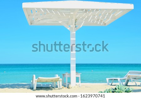 Village Olenevka Crimea. Nice white sand beach. Clear blue sea and sky background, big white wooden umbrella and plastic deck chair in shade. 