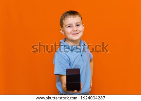 Attractive caucasian young boy in blue t-shirt holding black box present without a ribbon, for girl or mother, Valentines day, mother's day.Orange studio wall.