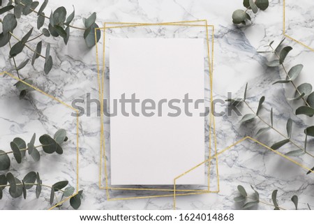Eucalyptus twigs and geometric golden frames on marble table with blank paper page. Abstract floral background. Flat lay, top view eucalyptus on white marble, flat lay on stone table, copy-space.