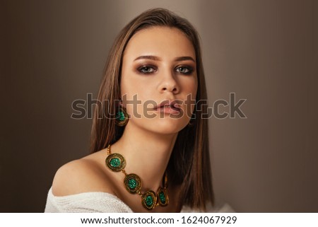 Fashion portrait of young beautiful girl with perfect smokey makeup wearing vintage jewelry. Teen model with elegant jewelery on brown background.
