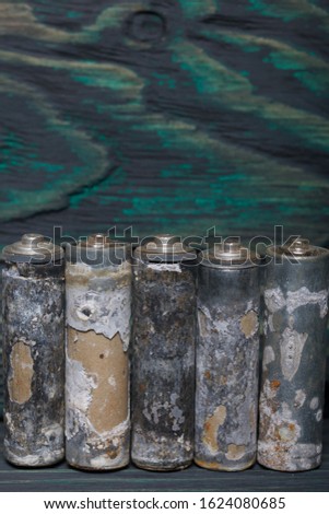 Corrosion finger batteries. Stand in a row. Against the background of brushed pine boards painted in black and green.