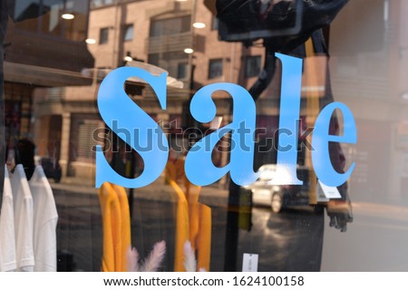 A sign in a shop window with blue lettering advertising a sale in store
