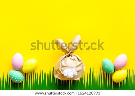 Easter concept. Eggs, decorative bunny and grass on yellow background top-down copy space