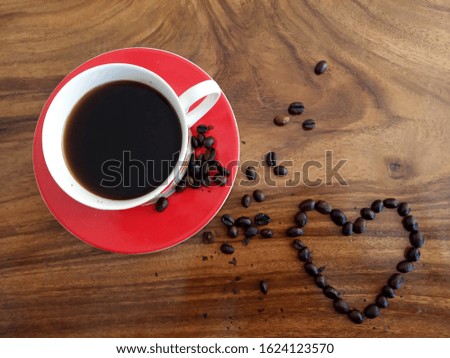 A cups of hot black coffee and love sign of raw coffee beans decoration. On wooden background table in high angle view, or top view. Food or drink flat lay concept. Copy space.