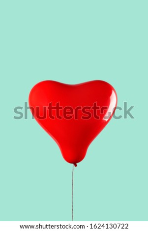 an inflated red heart-shaped balloon against a pale green or blue background with some blank space on top