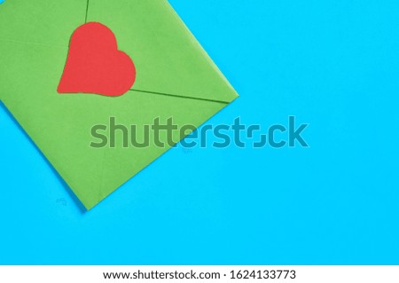 Closed green postal envelope and red paper heart on blue desk. Love message. Concept of Valentines Day. Space for text. Top view