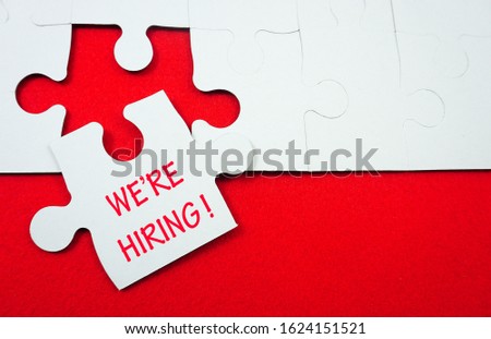 white jigsaw puzzle with word we're hiring over red background