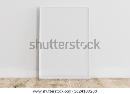 Empty thin white frame on light wooden floor with white wall behind it. Empty poster frame mockup. Empty picture frame mockup. Blank photo frame.