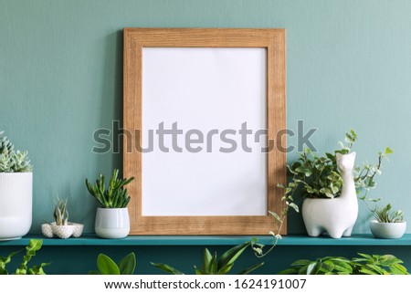 Interior design of living room with mock up photo frame on the green shelf with beautiful plants in different hipster and design pots. Elegant personal accessories. Home gardening. Template. 