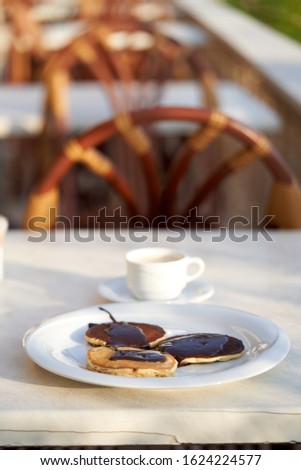  Freshly baked fritters poured with chocolate on a white plate, in the background is a glass of milk on a table in a cafe. Shallow depth of field, healthy breakfast                              