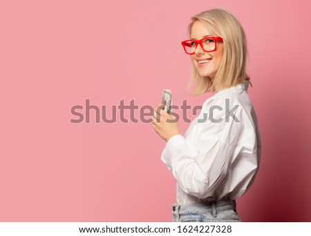 Beautiful blonde woman in glasses with dollars cash on pink background 