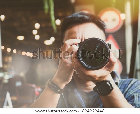 A male photographer wearing the smartwatch is holding a camera for taking a picture in the restaurant. Front view, close-up and color tone.