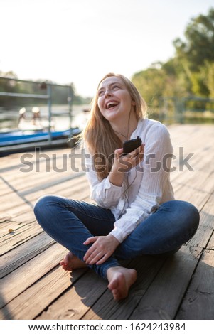 Beautiful girl sitting on wooden flor and listening to music at sunset