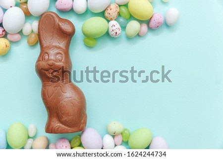 Happy Easter concept. Preparation for holiday. Easter candy chocolate eggs bunny and jellybean sweets isolated on trendy pastel blue background. Simple minimalism flat lay top view copy space