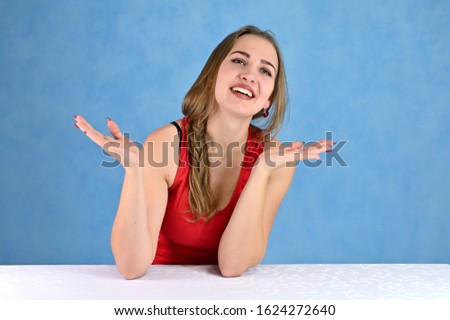 Universal concept female portrait on a blue background. Horizontal photo of a pretty smiling girl with long hair and great makeup sitting at a white table in the studio.