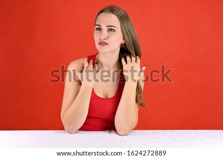 Universal concept female portrait on a red background. Horizontal photo of a pretty smiling girl with long hair and great makeup sitting at a white table in the studio.