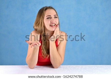 Universal concept female portrait on a blue background. Horizontal photo of a pretty smiling girl with long hair and great makeup sitting at a white table in the studio.