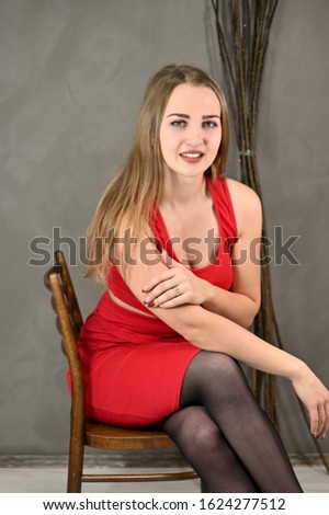 Vertical photo of a pretty smiling girl with long hair and excellent make-up in a red dress sitting on a chair in various poses. Universal concept female portrait on a gray background.