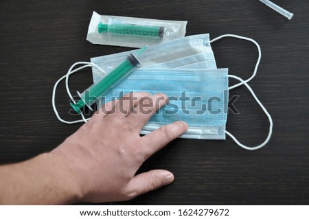 A male hand reaches for a medical syringe against the background of a protective mask against viruses. Virus prevention