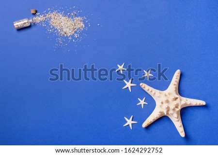 one big starfish and five small lying on a blue background in right corner and small bottle with sand in left corner, top view.