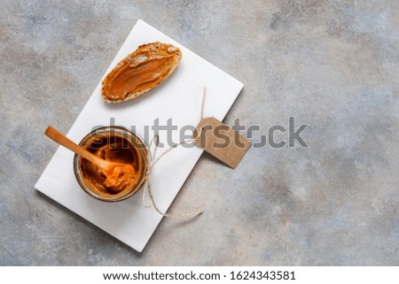 Glass jar of homemade salted caramel sauce with and bread . Close up, top view, background, flat lay
